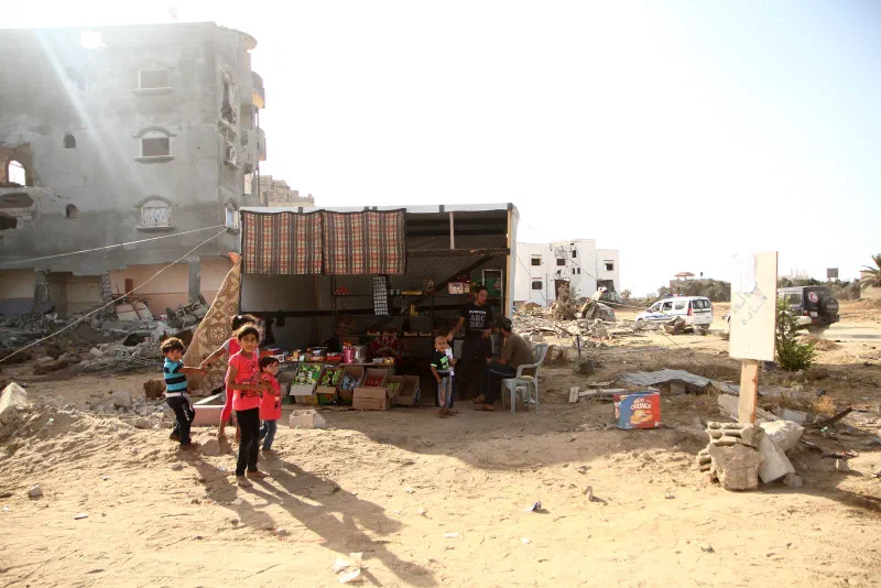 Children stand outside a small roadside shop among damaged buildings in the Gaza Strip.