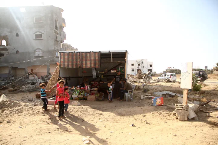 Children stand outside a small roadside shop among damaged buildings in the Gaza Strip.
