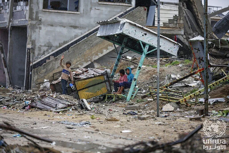 Displaced children sit beneath a collapsed shelter amid the rubble of their home in Nuseirat camp.
