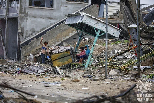 Displaced children sit beneath a collapsed shelter amid the rubble of their home in Nuseirat camp.