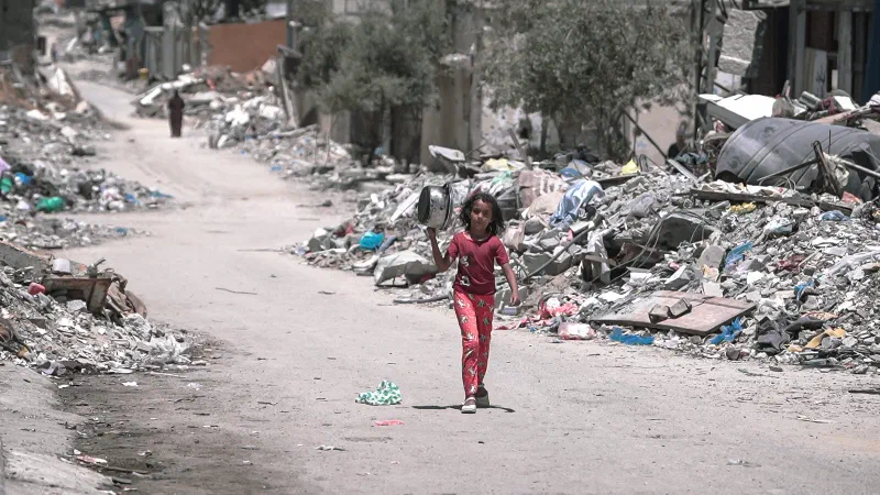 A girl carries a cooking pot along a rubble-lined street in Gaza.