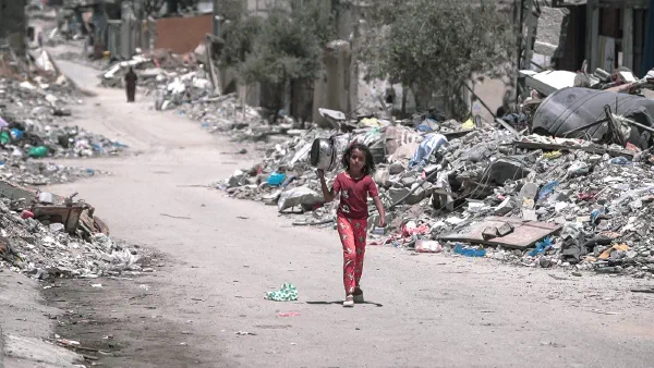A girl carries a cooking pot along a rubble-lined street in Gaza.